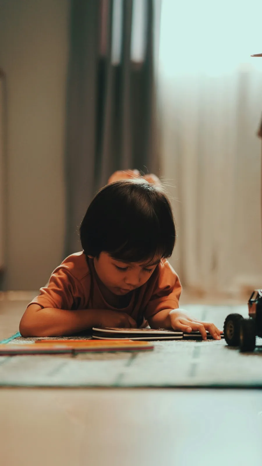 A young child lying on the floor, absorbed in drawing