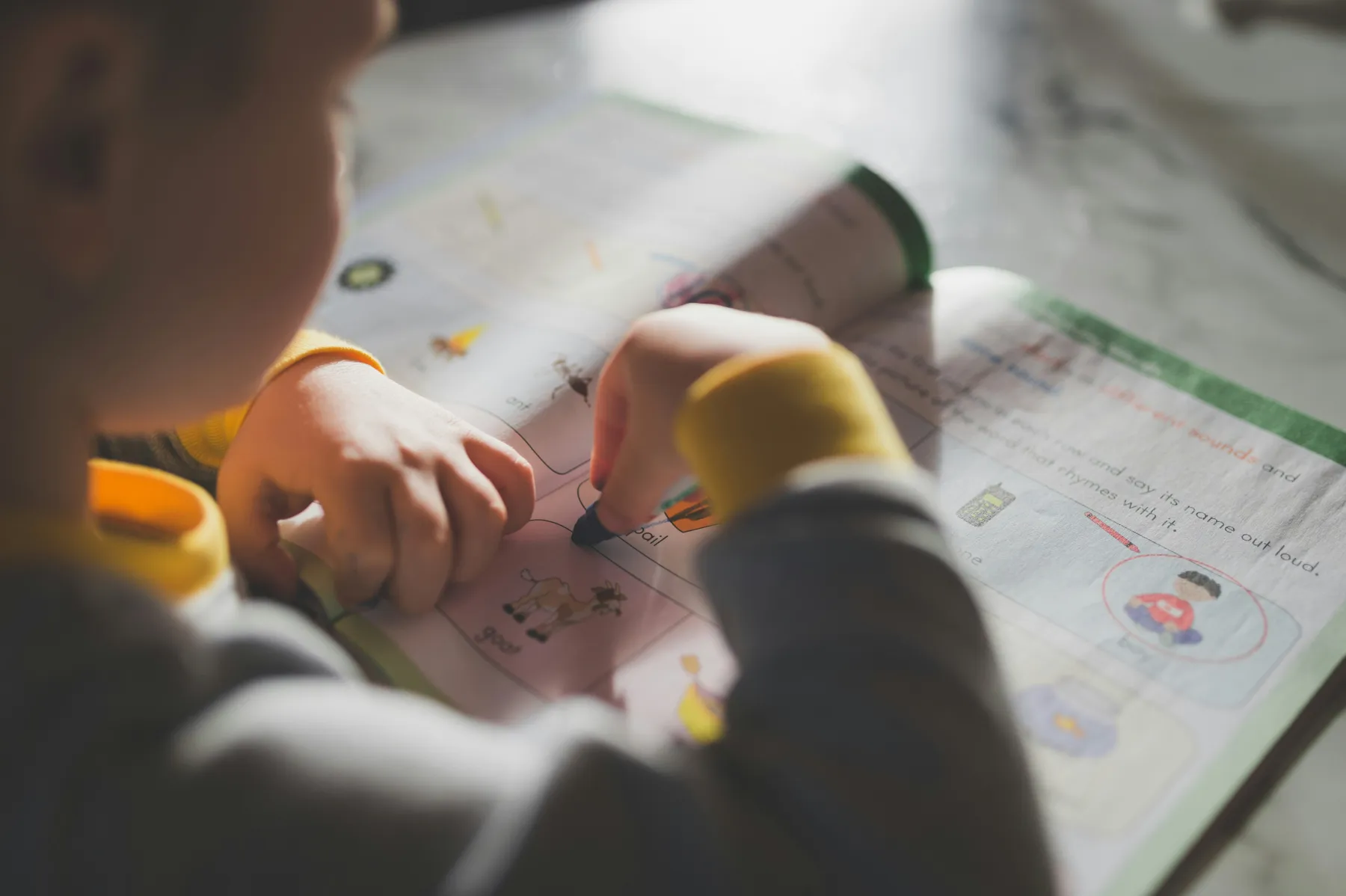 A child working through a picture-based exercise with a crayon